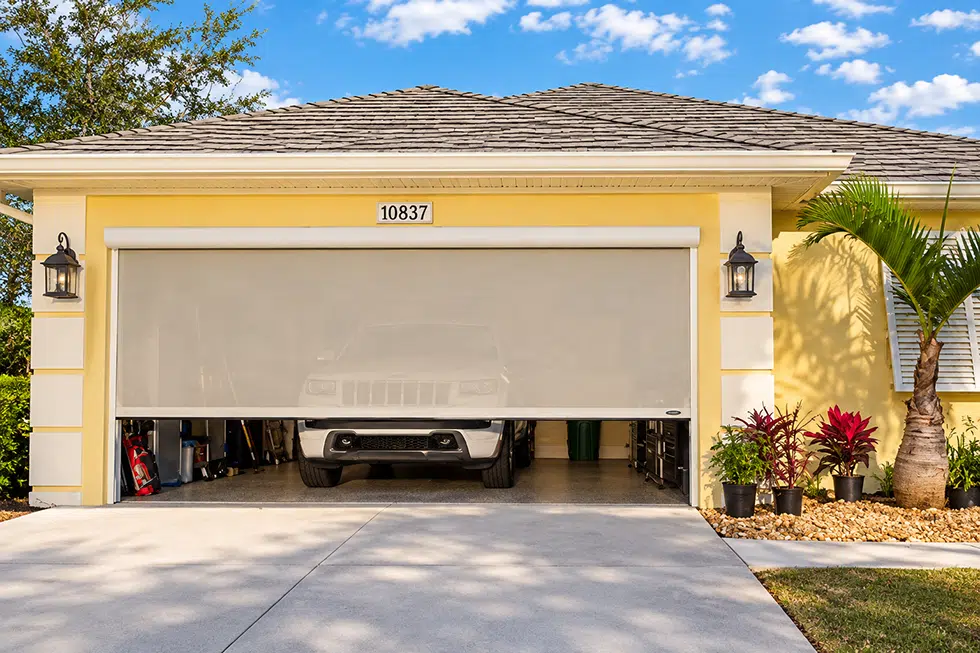 Motorized outdoor screen lowered across a residential garage opening with a vehicle visible behind the mesh